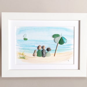May include: A framed watercolor painting of a family of four sitting on a beach with a green beach umbrella and a sailboat in the distance.