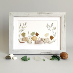 Peut inclure: Une œuvre d'art encadrée représentant des oiseaux en galets perchés sur des pierres. Les oiseaux sont de différentes couleurs, et l'œuvre est encadrée dans un cadre en bois blanc vieilli. Le fond est blanc, avec des accents floraux délicats.