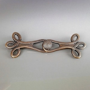 Peut inclure: Un fermoir en métal doré avec un motif de corde décoratif. Le fermoir est composé de deux pièces qui se connectent au milieu.