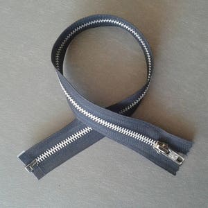 May include: A black zipper with silver teeth. The zipper is laid out in a figure of eight shape.