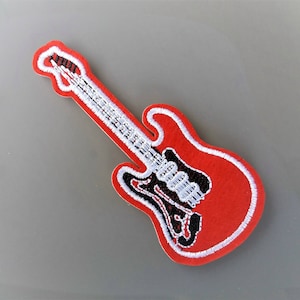 Peut inclure: Patch brodé de guitare rouge avec des détails blancs et noirs.