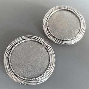 May include: Two silver-toned metal round picture frames with a decorative, textured, raised border. The frames are blank and ready for a photo or other embellishment.