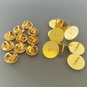 Peut inclure: Gros plan sur deux piles de dos de broches en métal couleur or. Les dos de broches sont ronds et ont une petite broche au dos. Il y a 15 dos de broches dans la pile de gauche et 7 dos de broches dans la pile de droite.