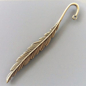 Könnte beinhalten: Ein goldfarbenes Metall-Lesezeichen in Form einer Feder. Das Lesezeichen hat oben eine Schlaufe zum Festhalten einer Seite.