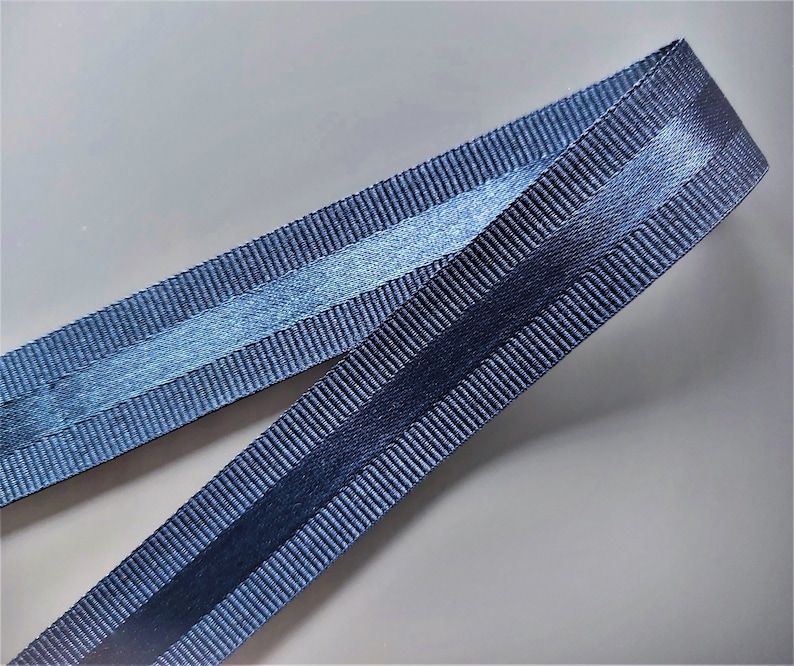Puede incluir: Una cinta azul oscuro con acabado satinado y una franja texturizada en el centro.