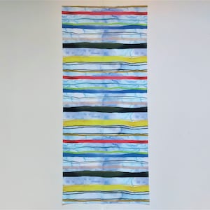 Peut inclure: Un long morceau de tissu étroit avec un motif répétitif de rayures colorées. Les rayures sont de différentes couleurs, notamment le bleu, le vert, le jaune, le rouge et le noir. Le tissu a un fond bleu clair.