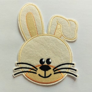 May include: A white felt bunny applique with black embroidered whiskers and brown eyes. The bunny has a small, orange embroidered mouth.