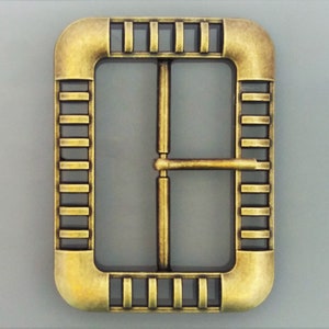 May include: A gold-toned metal buckle with a rectangular frame and a decorative patterned border. The buckle has a centre bar with a single hole for attaching a strap.