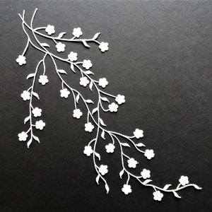 Op de afbeelding: Witte papieren uitsnijding van een delicate bloems tak met kleine bloesems op een zwarte achtergrond.