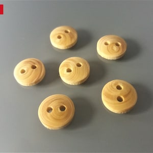 Può includere: Sei bottoni in legno con due fori ciascuno. I bottoni sono di colore marrone chiaro con una venatura del legno.
