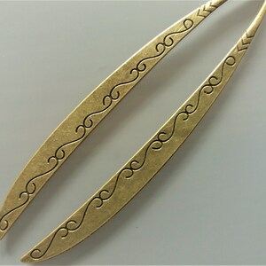 May include: Two gold-toned hair sticks with a decorative, swirling pattern. The sticks are long and slender, with a slightly curved shape.