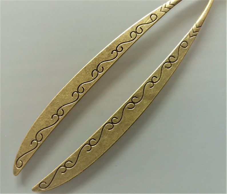 May include: Two gold-toned hair sticks with a decorative, swirling pattern. The sticks are long and slender, with a slightly curved shape.