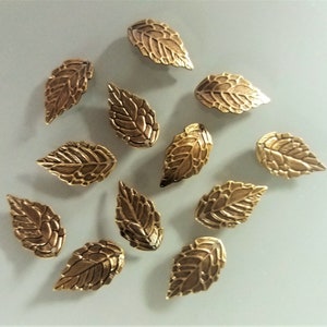May include: Twelve gold leaf-shaped metal embellishments. The leaves have a textured surface and are approximately 1 inch in length.