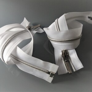 May include: Two white zipper tapes with silver teeth and sliders. The zippers are coiled and ready for sewing.