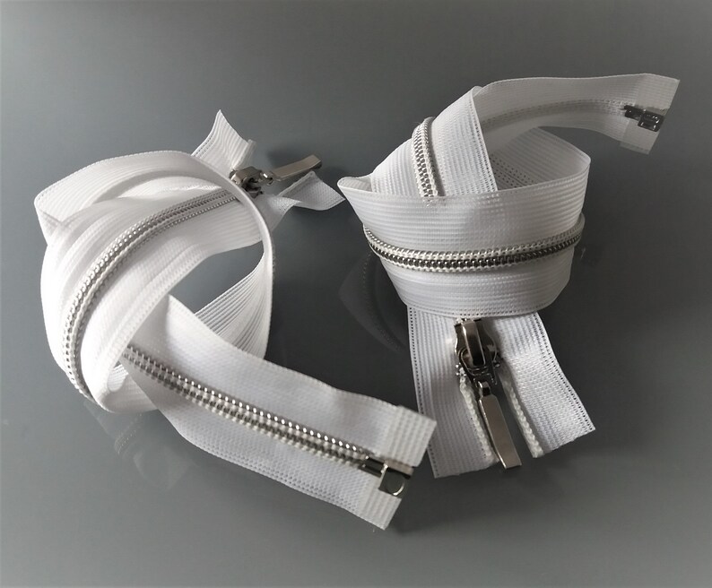 May include: Two white zipper tapes with silver teeth and sliders. The zippers are coiled and ready for sewing.