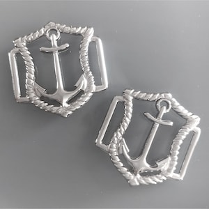 Peut inclure: Deux breloques d'ancre en métal argenté avec un motif de corde. Les ancres sont en relief et entourées d'une bordure en forme de corde.