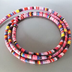 May include: A colourful, multi-striped cord with pink, red, yellow, blue, and black stripes. The cord is made of woven fabric and is approximately 1.2 cm wide.
