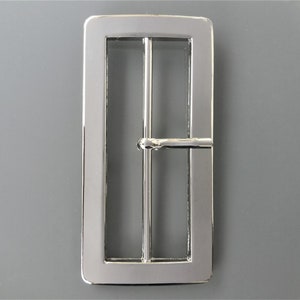 May include: A silver metal belt buckle with a rectangular shape and a smooth finish.
