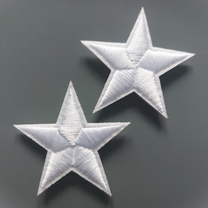 Op de afbeelding: Twee witte geborduurde sterrenpatches. Elke ster heeft vijf punten en is gevuld met wit garen. De sterren staan op een grijze achtergrond. Deze patches kunnen worden gebruikt om kleding, tassen of andere stoffen items te versieren.