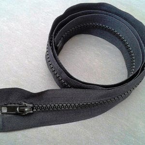 Può includere: Nastro di cerniera lampo nero con cursore in metallo. La cerniera lampo è arrotolata e pronta per essere cucita su un capo di abbigliamento.