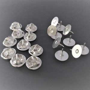 May include: A set of silver-toned metal pin backs for attaching badges, pins, or other small items to clothing or fabric. The set includes both round and flat pin backs.