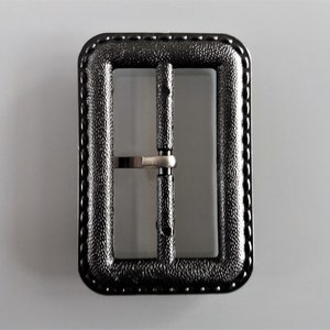 May include: Black metal belt buckle with a textured finish and a stitched edge.