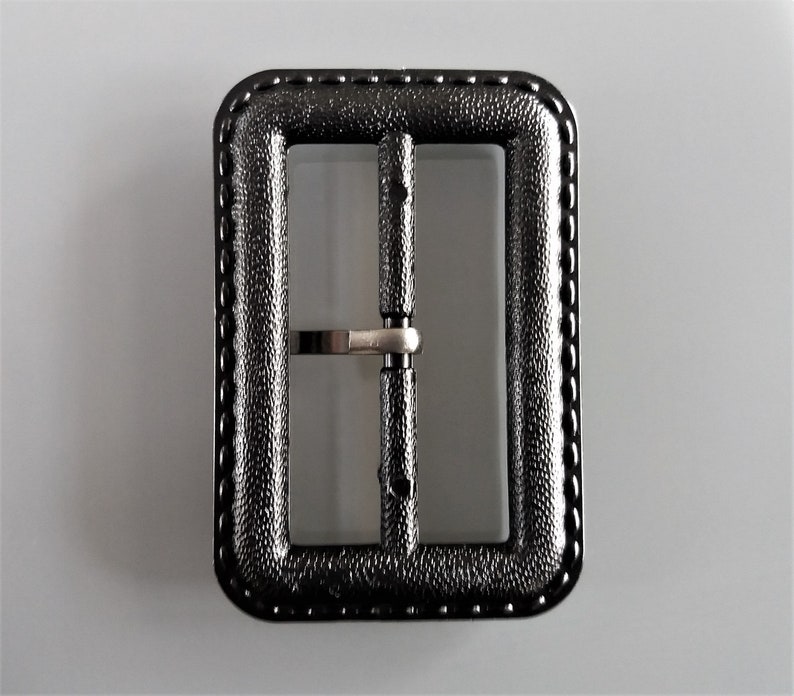 May include: Black metal belt buckle with a textured finish and a stitched edge.