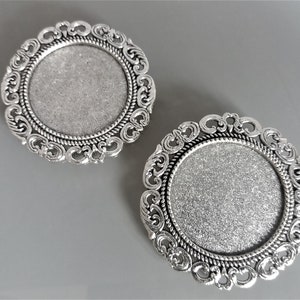 May include: Two silver-toned metal round decorative embellishments with ornate filigree designs. The embellishments have a smooth, silver-toned surface and a raised, circular centre.