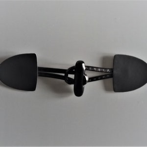Könnte beinhalten: Schwarzer Toggle-Verschluss mit zwei schwarzen, abgerundeten, ovalen Teilen, die durch ein schwarzes Band verbunden sind.