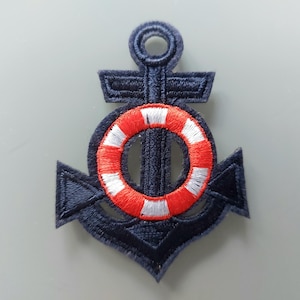 Op de afbeelding: Geborduurd marineblauw ankerpatch met een rood-witte reddingsboei in het midden. De patch heeft een getextureerde uitstraling en is waarschijnlijk bedoeld om op kleding of accessoires te worden genaaid. Nautisch thema.