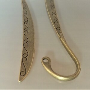 May include: Two antique gold-toned metal bookmarks. One bookmark is a simple curved shape with a decorative design. The other bookmark is a curved shape with a hook at the end.