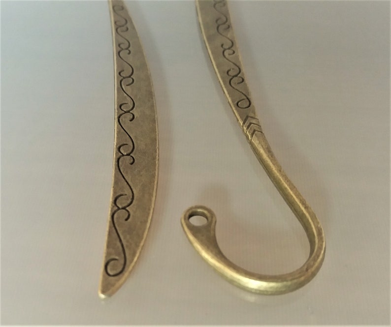 May include: Two antique gold-toned metal bookmarks. One bookmark is a simple curved shape with a decorative design. The other bookmark is a curved shape with a hook at the end.