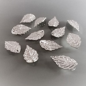 Op de afbeelding: Een verzameling zilverkleurige metalen bladerencharms. De bladeren zijn gedetailleerd met nerven en hebben een licht getextureerd oppervlak.