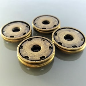 May include: Four antique brass-coloured snap fasteners. Each fastener has a circular design with a central hole and several smaller holes around the edge. The fasteners are slightly tarnished, giving them a vintage look.