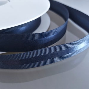 Puede incluir: Un carrete de cinta de grosgrain azul oscuro con una raya de sat&eacute;n en el centro.