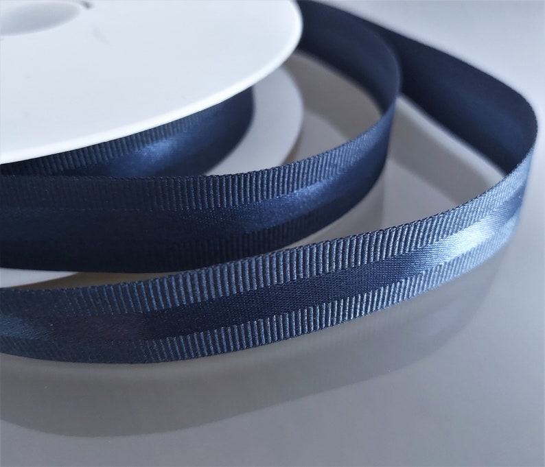 Puede incluir: Un carrete de cinta de grosgrain azul oscuro con una raya de sat&eacute;n en el centro.