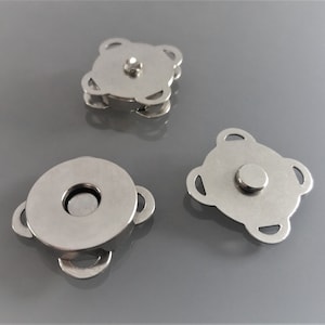 May include: Three silver magnetic snap closures. The closures are designed to be sewn onto fabric. The closures are round, square, and round with a centre hole.