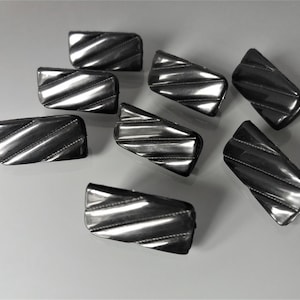 Op de afbeelding: Een set van acht zwarte rechthoekige plastic knoppen met een diagonaal geribbeld patroon.