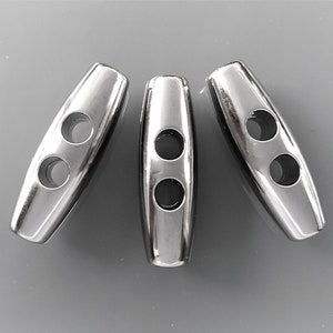Op de afbeelding: Drie zilveren metalen toggles met elk twee gaten. De toggles zijn glad en glanzend.