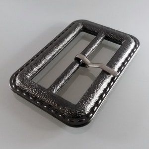 May include: A black metal buckle with a textured finish and a silver metal slider. The buckle has a stitched edge.
