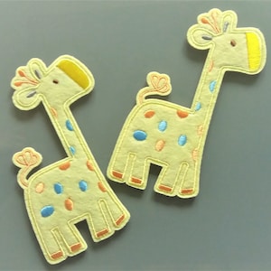 May include: Two light yellow giraffe applique patches. Each giraffe has a long neck, orange, blue, and yellow spots, and a yellow head. The patches are made of felt and have embroidered details.
