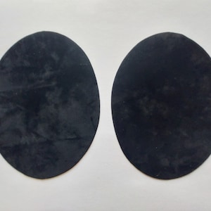 Könnte beinhalten: Zwei schwarze, runde Filzpads. Die Pads sind glatt und haben eine leicht strukturierte Oberfläche.