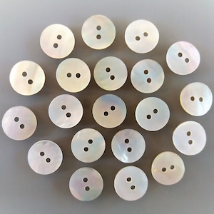 Peut inclure: Un ensemble de boutons ronds en nacre irisée, chacun percé de deux trous. Les boutons sont d'un blanc crémeux avec de subtiles nuances arc-en-ciel, parfaits pour la couture ou pour décorer des vêtements.