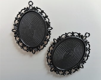 May include: Two black metal oval-shaped pendant trays with ornate filigree designs around the edges. The trays are blank and ready to be filled with resin, photos, or other embellishments.