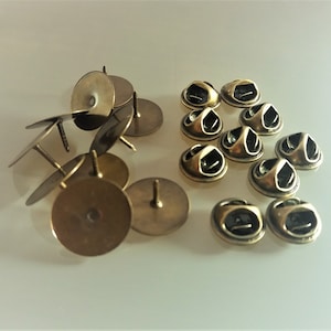 Pode incluir: Um conjunto de 12 costas de alfinete de metal dourado. As costas de alfinete são redondas e têm um pequeno furo no centro. As costas de alfinete são usadas para prender alfinetes a roupas ou outros itens.