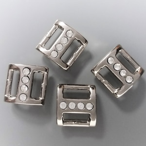 Peut inclure: Quatre boucles en métal argenté avec des accents de strass transparents. Chaque boucle a deux trous pour la fixation à une sangle ou une ceinture.