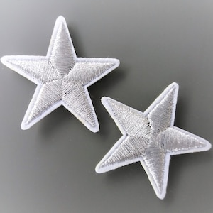 Op de afbeelding: Twee zilveren glittersterren strijklabels. De sterren hebben een witte omtrek.