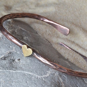 May include: A hammered copper bangle bracelet with a small gold heart charm.