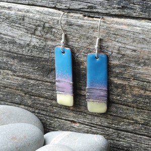 May include: A pair of dangle earrings with a blue, purple and yellow enamel design. The earrings are made of metal and have a silver finish.