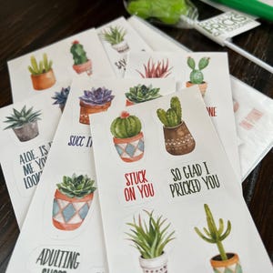 May include: A selection of white stickers with watercolour illustrations of cacti and succulents in pots. Some stickers have phrases such as "Stuck on You" and "So Glad I Pricked You".